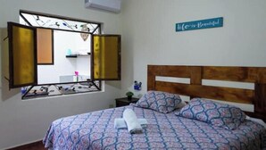 Ein Schlafzimmer mit einem Bett, einem Fenster mit geöffneten Läden, einem Wandzeichen und einem kleinen Nachttisch.