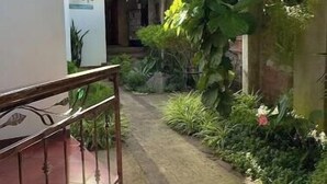 A pathway leading to a building with a balcony and a garden area with various plants. - 103 Apartment in Villa Stahl, Colonia Escalon (San Salvador)