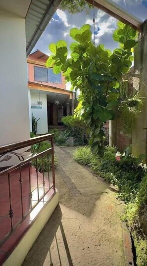 Ein Weg führt zu einem Gebäude mit Balkon und einem Gartenbereich mit verschiedenen Pflanzen.