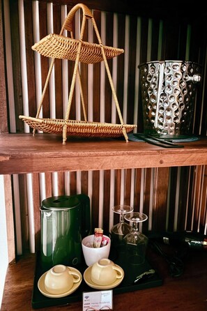 Een rieten stoel, een decoratieve metalen pot, een groene thermoskan, twee theekopjes en een bordje met een WiFi-toegangscode.