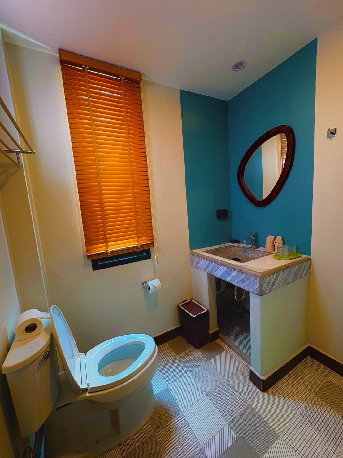 A bathroom with a toilet, sink, mirror, and window with blinds.