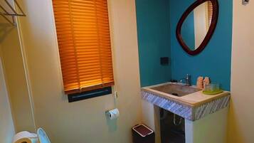 A bathroom with a toilet, sink, mirror, and window with blinds.