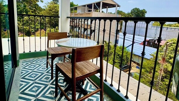 A balcony with a table and chairs, a patterned floor, and a view of a body of water and buildings. - Mersey Residence Koh Samui (Koh Samui)