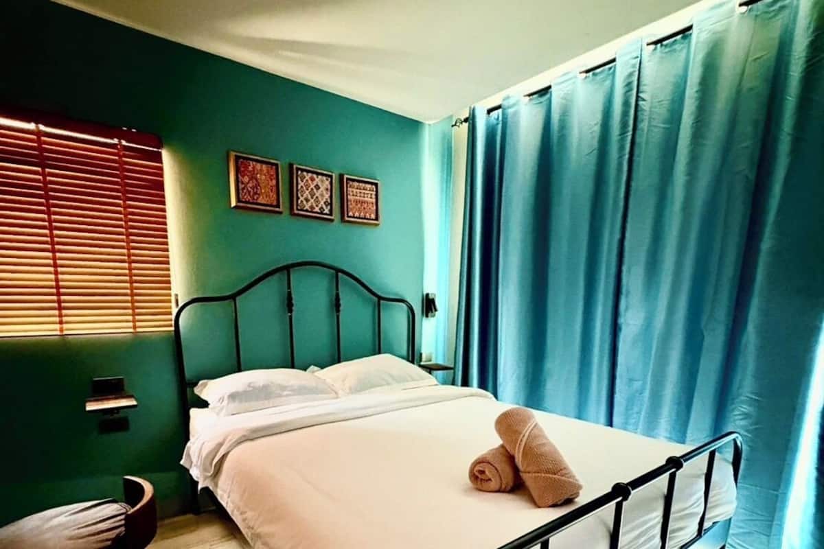 A single bed with white bedding, a wooden chair, and a window with blinds.