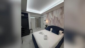 A modern bedroom with a large bed, a walk-in closet, and a shower area. - Della Vite Home Collection (Rome)