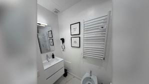 A modern bathroom with a white sink, mirror, and bidet. There are framed pictures on the wall and a towel rack. - Della Vite Home Collection (Rome)