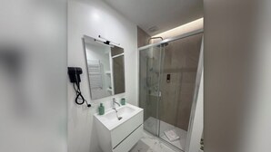 A modern bathroom with a white vanity, a glass shower enclosure, and a visible hairdryer on the wall. - Della Vite Home Collection (Rome)