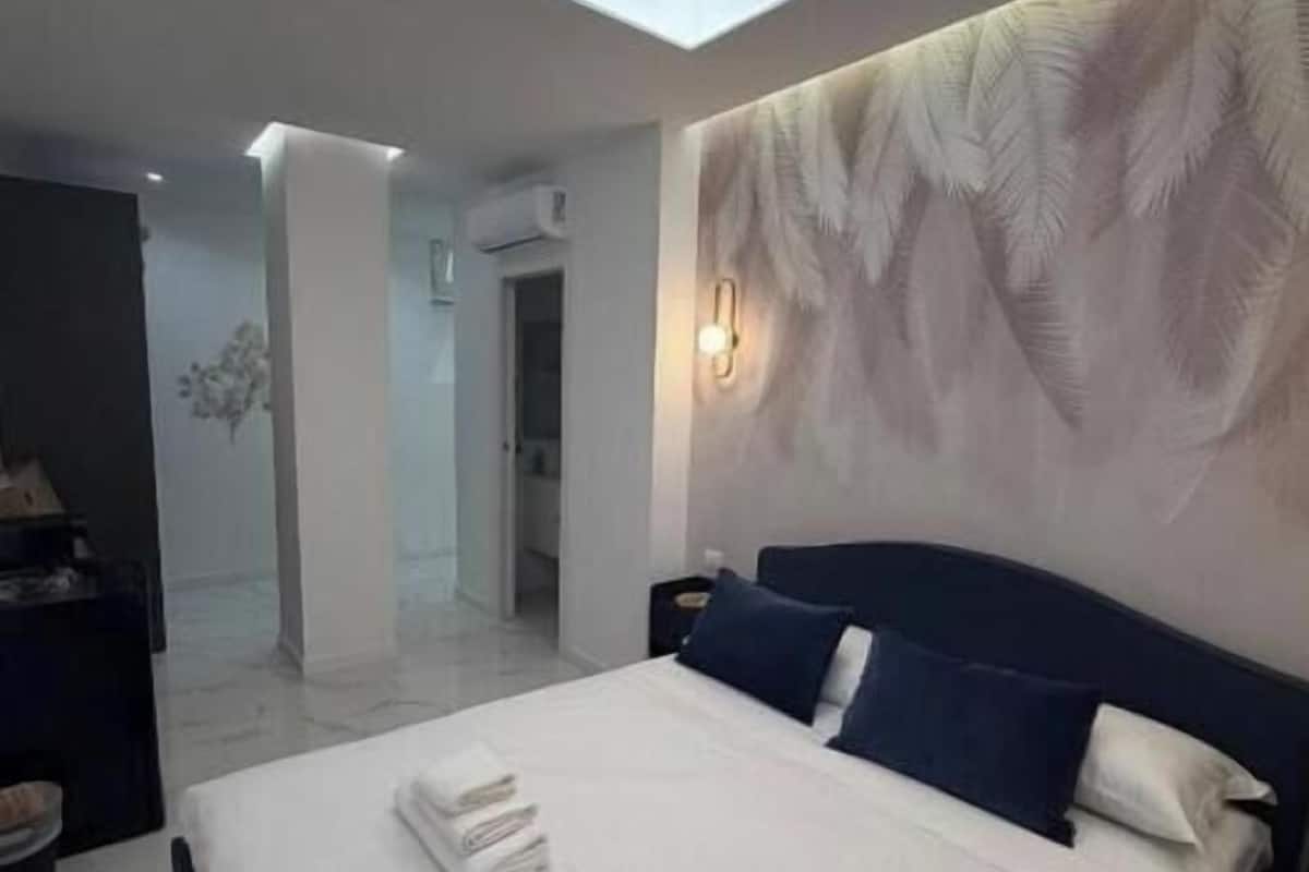Un dormitorio moderno con tragaluces, una cama con almohadas, una mesita de noche y una pared con diseño de hojas.