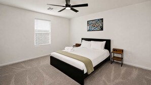 A bedroom with a bed, a ceiling fan, a window with blinds, a bedside table, and a nightstand. - Spacious 4BR Rental near Downtown Prescott (Prescott Valley)