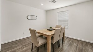 A dining area with a wooden table and four chairs, a small potted plant, and a window with blinds. - Spacious 4BR Rental near Downtown Prescott (Prescott Valley)