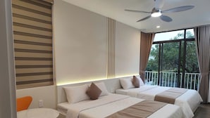 Quarto de hotel com duas camas, ventoinha no teto, varanda com cortinas e uma pequena mesa com cadeira.