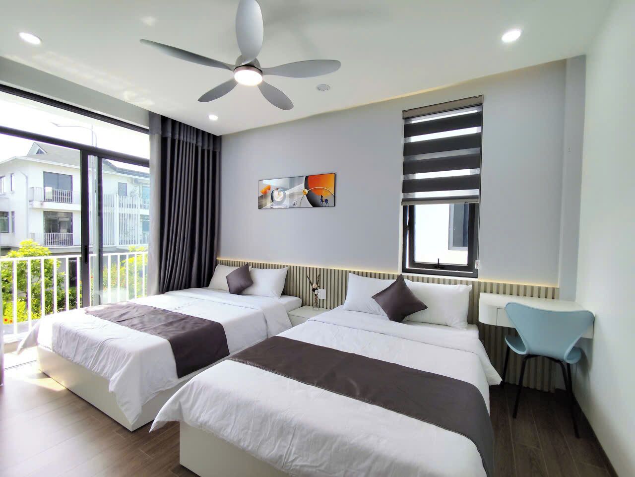 A hotel room with two beds, a ceiling fan, a desk, and a view of the outside.