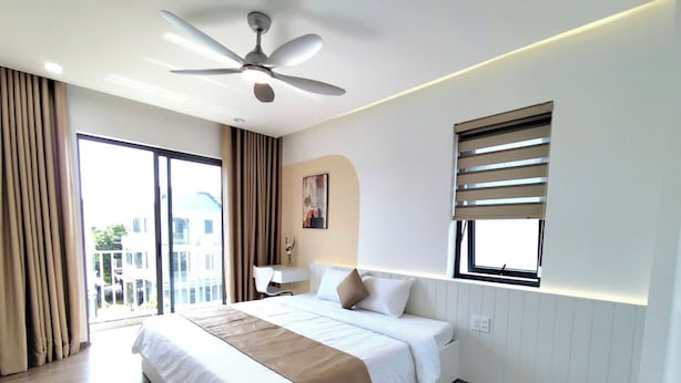 Quarto de hotel moderno com uma cama grande, um ventilador de teto, uma janela com persianas e vista para o exterior.
