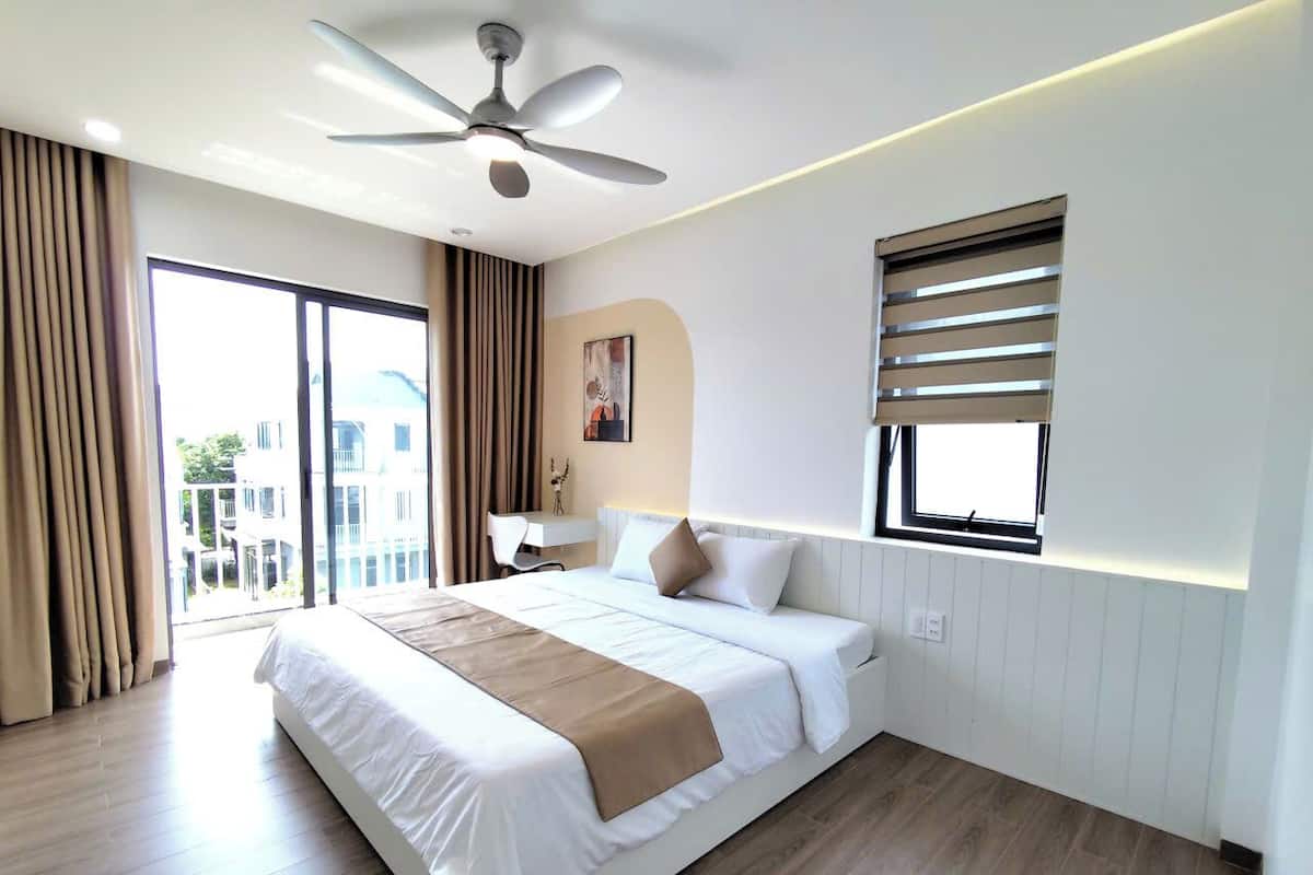 Una habitación de hotel moderna con una cama grande, un ventilador de techo, una ventana con persianas y vistas al exterior.