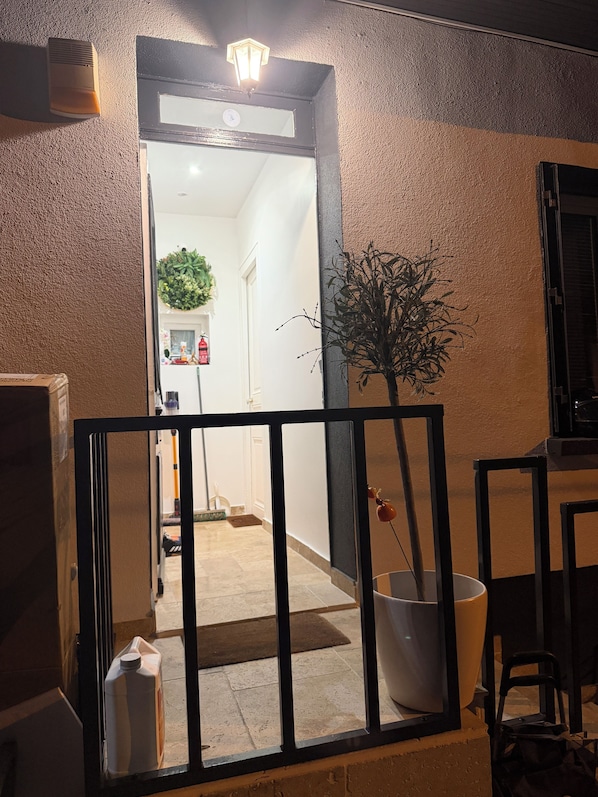 Een deuropening naar een kamer met een potplant, een witte emmer en een grote witte bak.