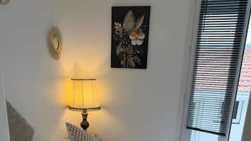 A bedroom with a bed, pillows, a bedside lamp, a wall art piece, and a window with blinds.