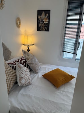 Une chambre à coucher avec un lit, des oreillers, une lampe de chevet, un tableau décoratif au mur et une fenêtre avec des stores.