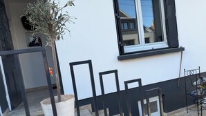 Un edificio blanco con un marco de ventana negro, una planta en maceta y una silla metálica.