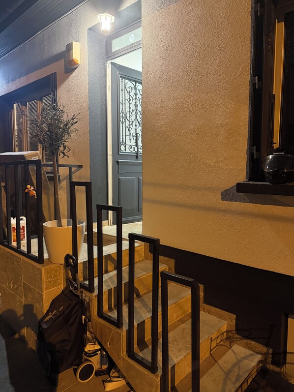 Una escalera conduce a una puerta con una reja de hierro decorativa, una planta en maceta y un bolso en los peldaños.