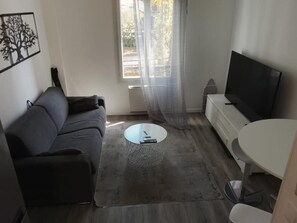 Olohuoneessa on sohva, sohvapöytä, televisio ja ikkuna, jossa on läpikuultavat verhot.