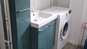A compact laundry room with a washing machine, a sink, and a green rug on the floor. - Cosy air-conditioned apartment 5 minutes from the sea (Nice)