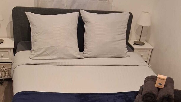 A bed with a dark blue blanket, white pillows, and a folded towel on the side. - Cosy air-conditioned apartment 5 minutes from the sea (Nice)