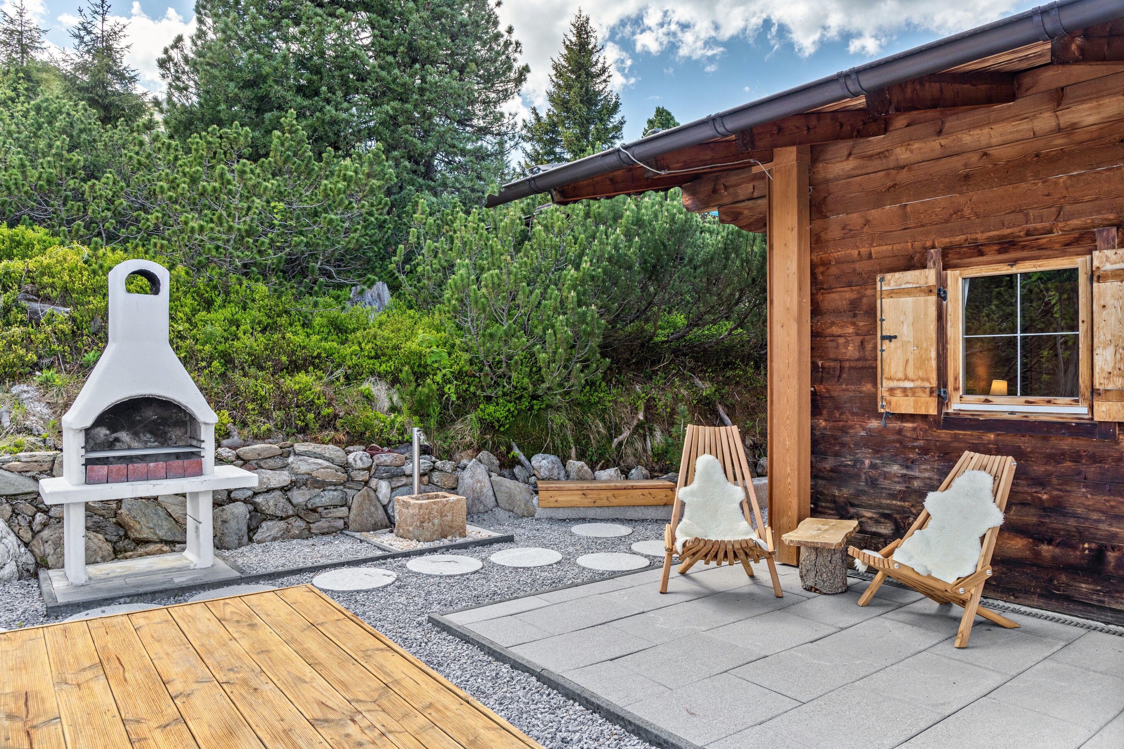 A wooden cabin with a stone fireplace, two Adirondack chairs, and a deck.