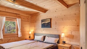 A wooden cabin room with a bed, two bedside lamps, a window with curtains, and a framed picture on the wall. - Chalet 'Hochzillertal' with Mountain View, Private Terrace and Wi-Fi (Kaltenbach)