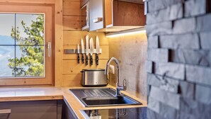 A kitchen with wooden cabinets, a stainless steel toaster, a sink with a faucet, and a window with a view of trees. - Chalet 'Hochzillertal' with Mountain View, Private Terrace and Wi-Fi (Kaltenbach)