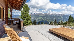 A wooden cabin with a deck, outdoor seating, and a view of snow-capped mountains. - Chalet 'Hochzillertal' with Mountain View, Private Terrace and Wi-Fi (Kaltenbach)
