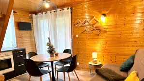 Et hyggeligt sommerhusinteriør med spiseplads, sofa og et lille bord med lampe.