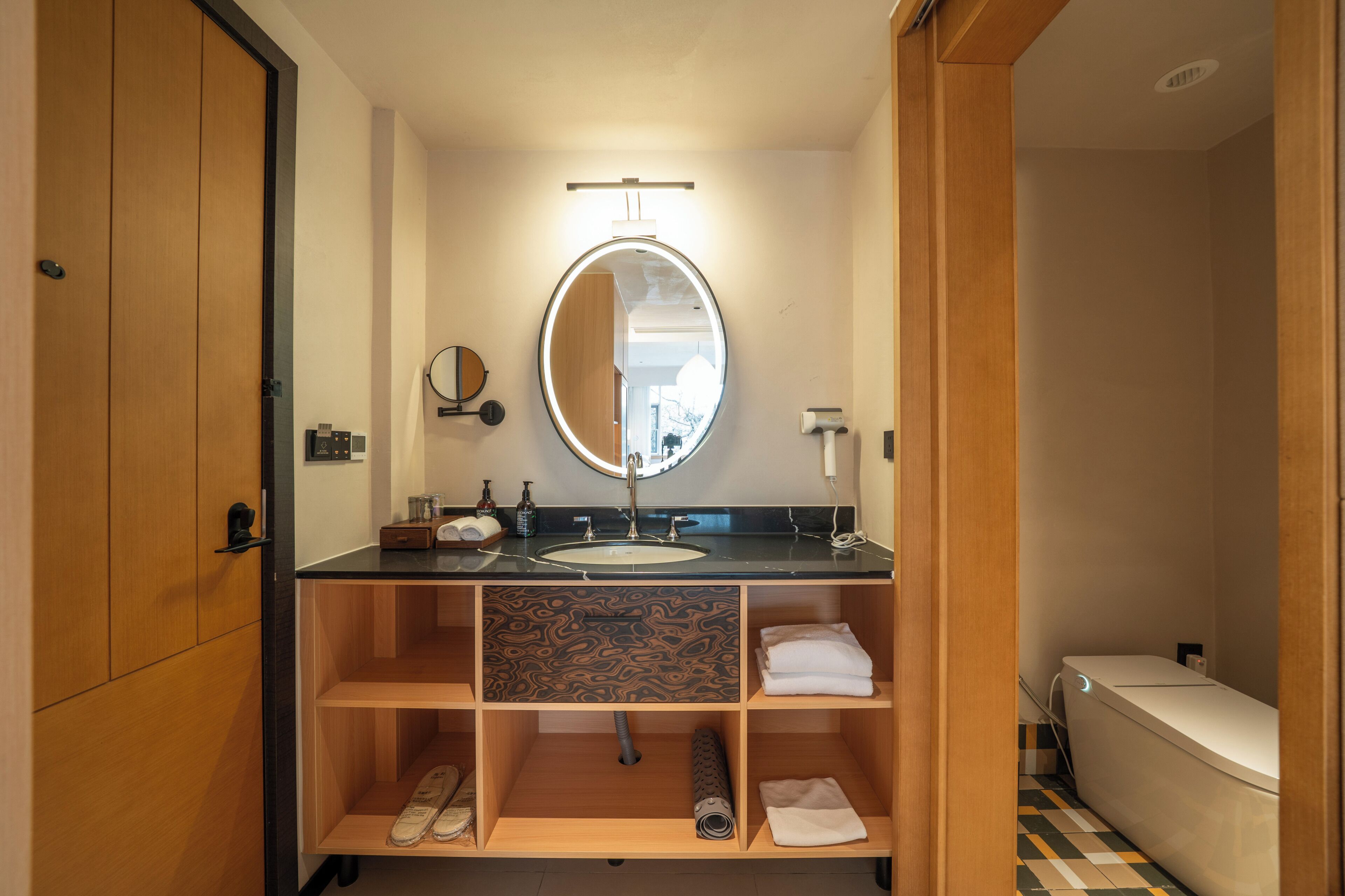 Un baño moderno con tocador de madera, un espejo redondo, un lavabo e inodoro.