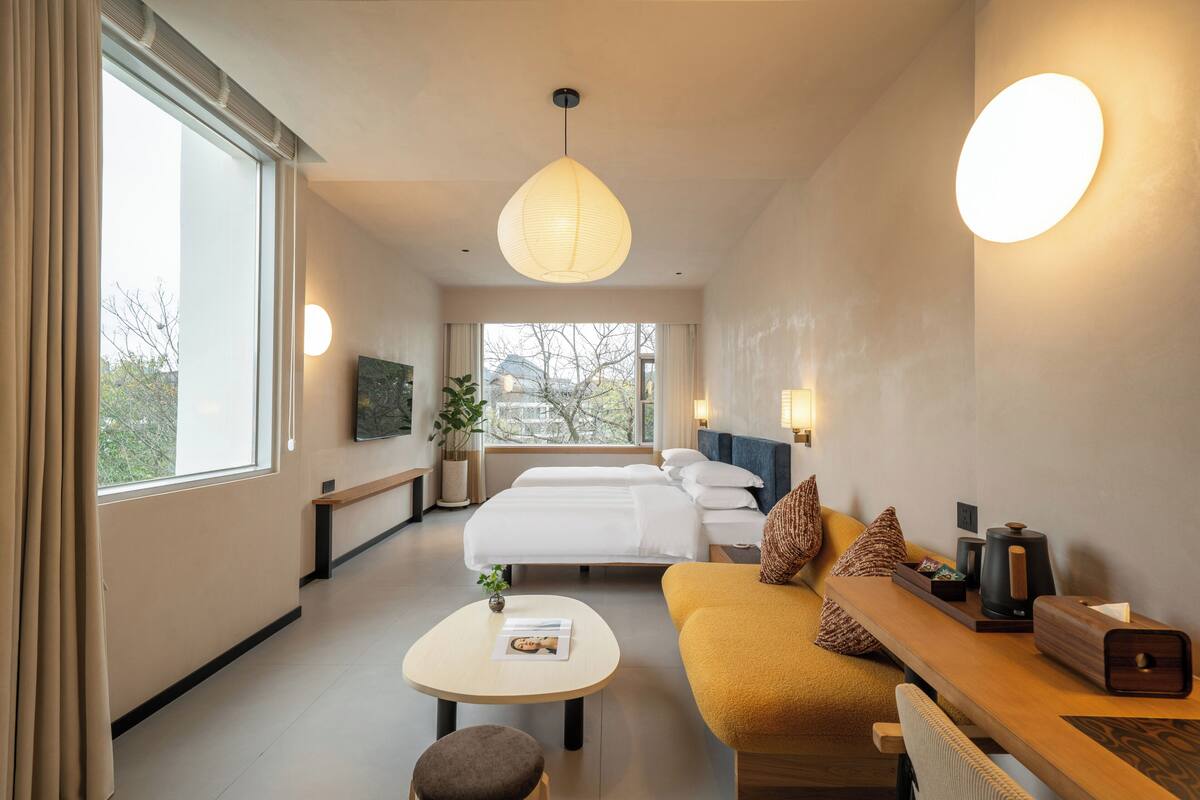 Una habitación de hotel con cama, sofá, mesa de centro, televisor y ventana con cortinas.