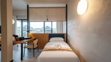 A hotel room with a bed, a desk, a chair, a lamp, and a view of mountains through the window.