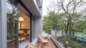 Un balcón moderno con mobiliario de madera, un ventanal de vidrio que da a una habitación y vistas a árboles, además de un cartel que prohíbe subir.