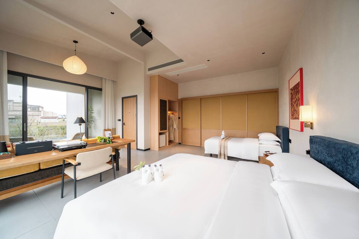Una habitación de hotel moderna con una cama grande, un escritorio con una computadora portátil, una silla y vistas a la ciudad a través de amplios ventanales.
