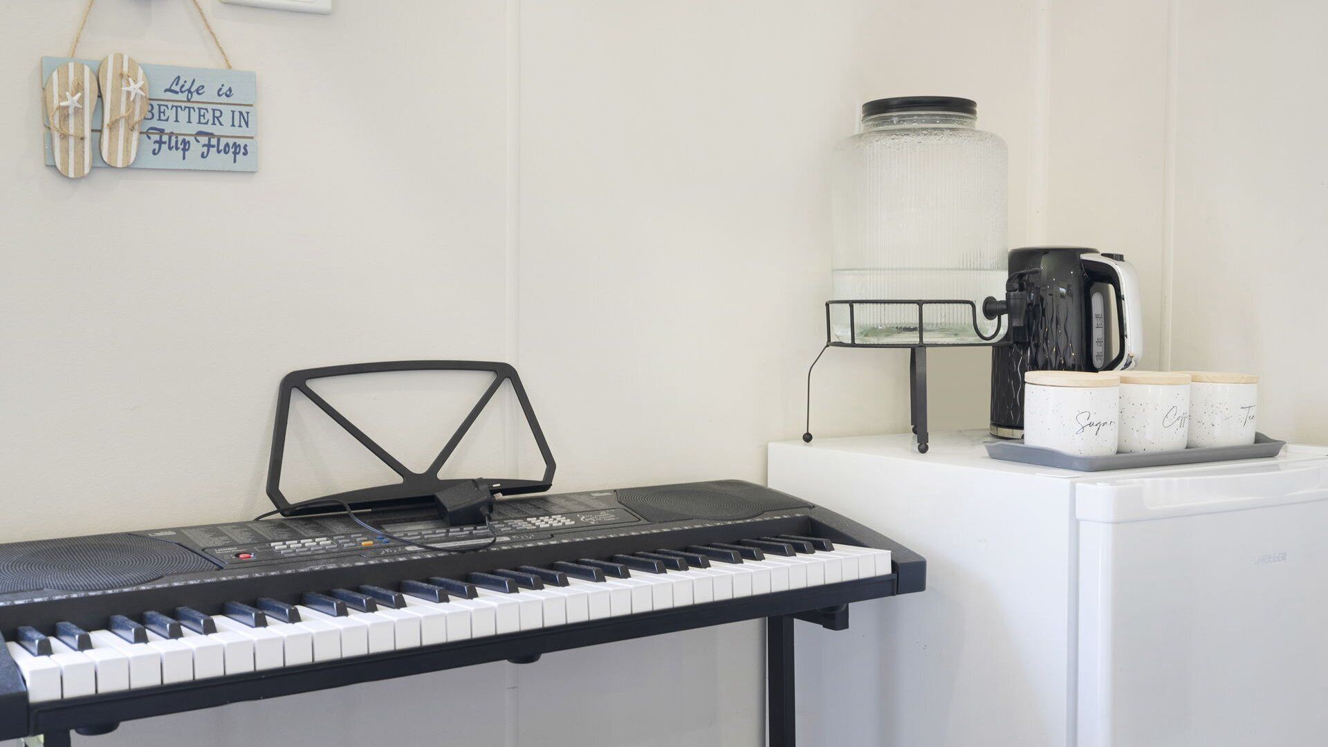 A room with a keyboard, a coffee maker, and a jar of sugar on a counter.