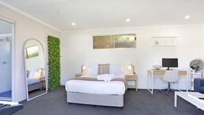 A modern bedroom with a bed, bedside tables, a desk, a chair, a mirror, and a green wall.