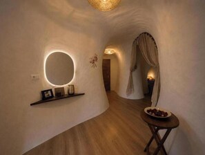 A hallway with a round mirror, a small table with a bowl of fruit, and a door with a curtain. - Jardines de Ifonche – 2-Bedroom Cave House in Tenerife (Adeje)