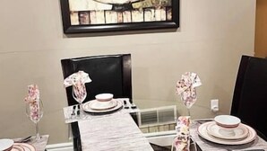 Un coin repas avec une table dressée pour quatre personnes, agrémentée d’une nappe en marbre, d’assiettes blanches et de serviettes à motifs floraux.