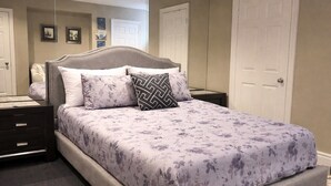 Une chambre à coucher comprenant un lit, des tables de chevet, une commode, un miroir et une porte.