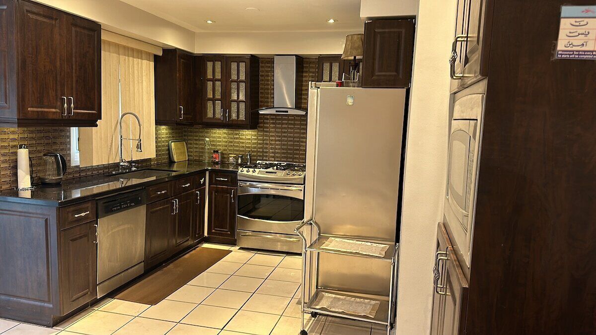 A kitchen with dark wooden cabinets, a stainless steel refrigerator, a stove, and a dishwasher.