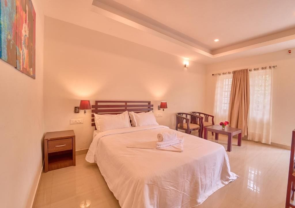 Une chambre d’hôtel avec un grand lit, des lampes de chevet, une petite table avec une chaise et un tableau au mur.