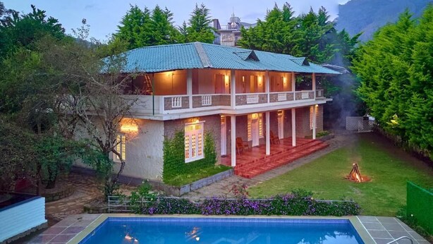 Una casa de dos pisos con piscina, rodeada de follaje y montañas al fondo.