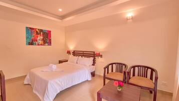 A hotel room with a bed, two chairs, a small table with a vase, and a painting on the wall.