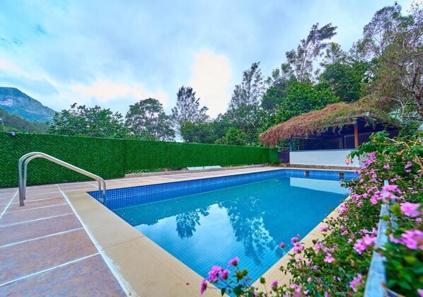 Una piscina con barandilla de metal, rodeada por un seto verde y una estructura con techo de paja.
