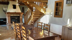 A dining area with a wooden table and chairs, a fireplace, and a staircase. - Charming country cottage with fireplace near Rouen and the Normandy coast (Auzouville-l'Esneval)