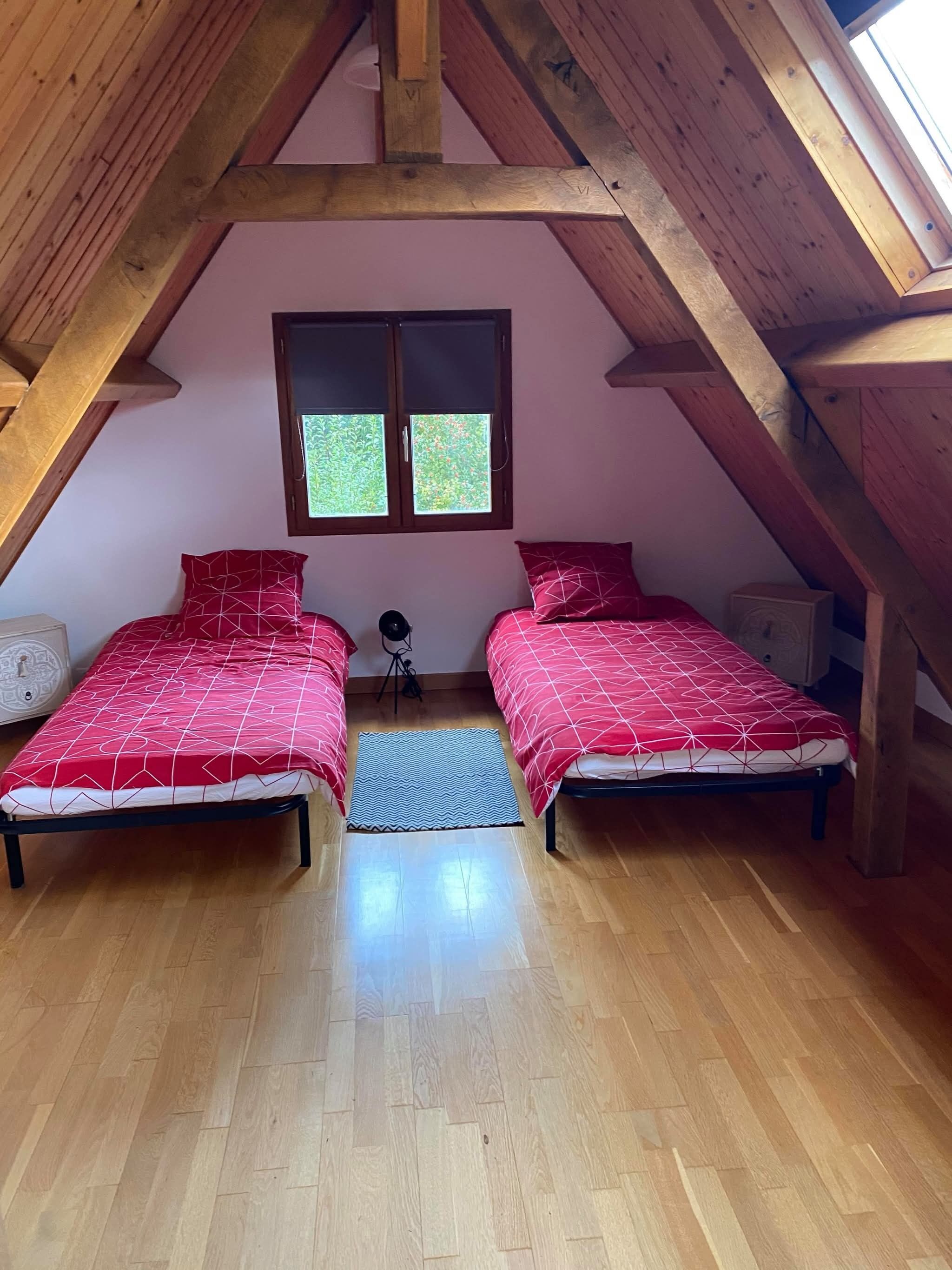 A bedroom with two beds, a window, wooden beams, and a small rug.