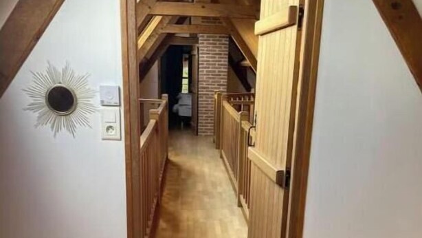 A narrow hallway with wooden flooring and a sloped ceiling, leading to a room with a brick wall and a door. - Charming country cottage with fireplace near Rouen and the Normandy coast (Auzouville-l'Esneval)