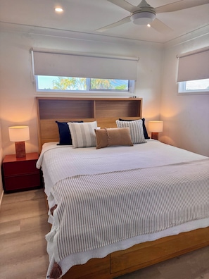 A bedroom with a bed, nightstands, a ceiling fan, and windows.